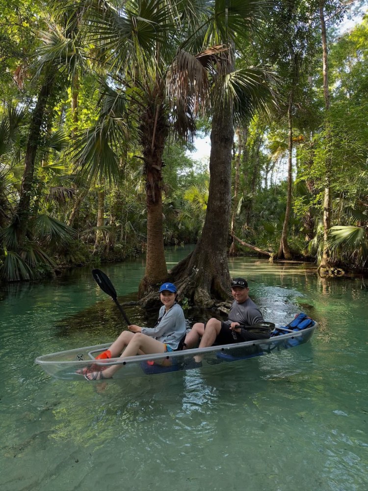 Two people kayaking in a clear turquoise river surrounded by lush greenery.