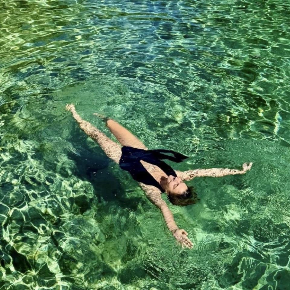 Person in a swimsuit floating in clear green water, arms outstretched.