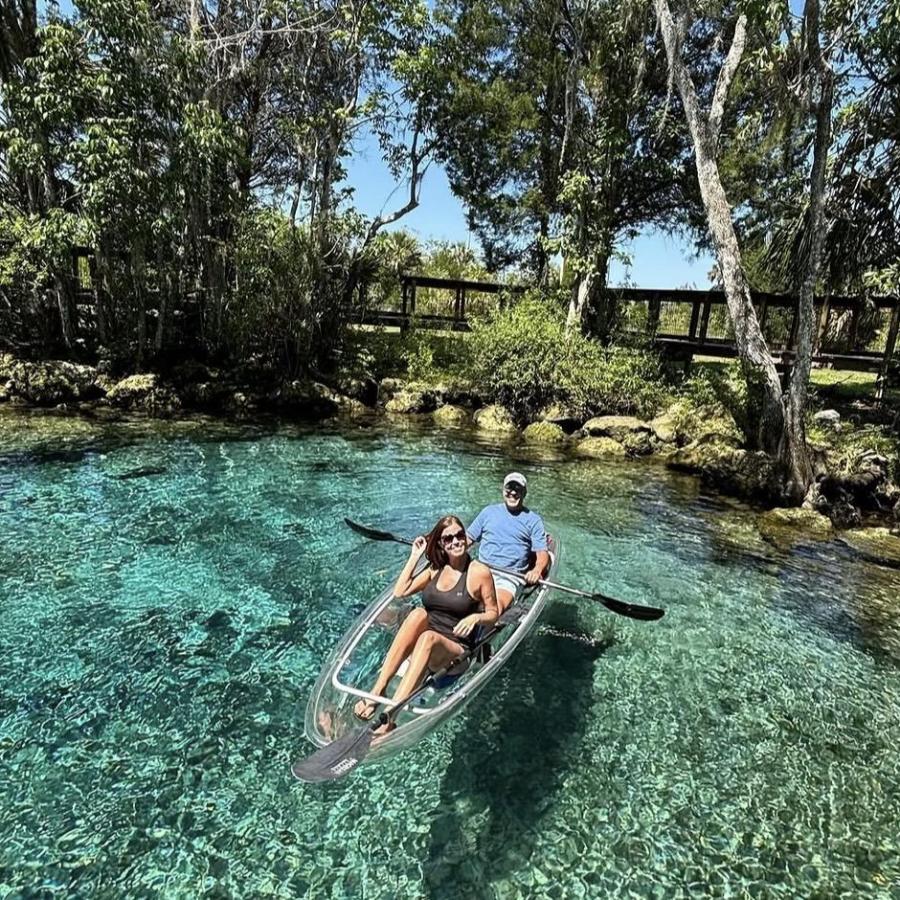 Two people kayaking on clear water surrounded by trees and sky.