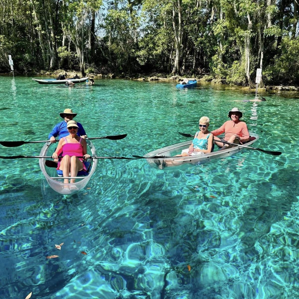 Two kayaks with people floating on clear water near a forested shore.