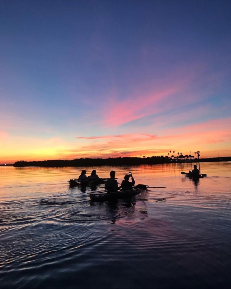 People kayaking on a calm lake at sunset with pink and orange sky.