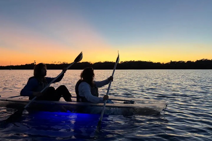 Two people kayaking on a lake at sunset with glowing kayaks.