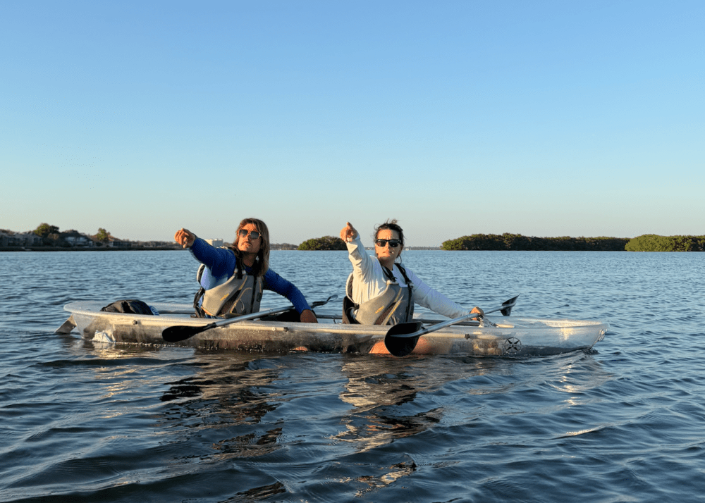 Two people kayaking on calm water, pointing ahead.