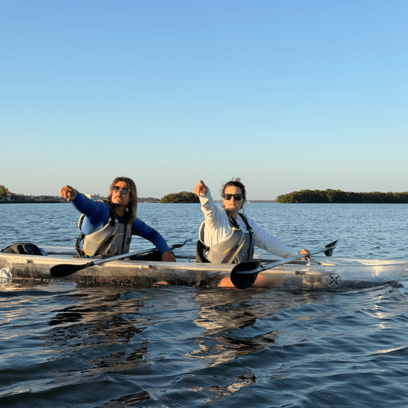 Two people kayaking on calm water, pointing ahead.