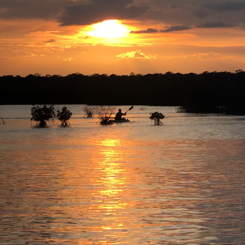 Person kayaking on a lake during sunset with cloudy sky.