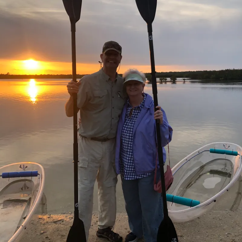 Couple holding kayak paddles by a lake at sunset.
