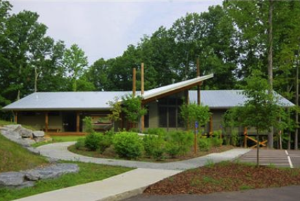 Modern building with sloped roof, surrounded by trees and a landscaped path.
