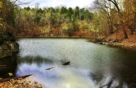 Small lake with surrounding bare trees and rocky shoreline.