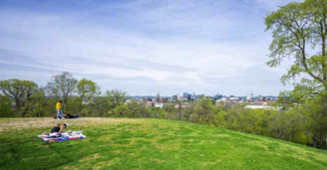 People relaxing on grass with a city skyline in the distance.