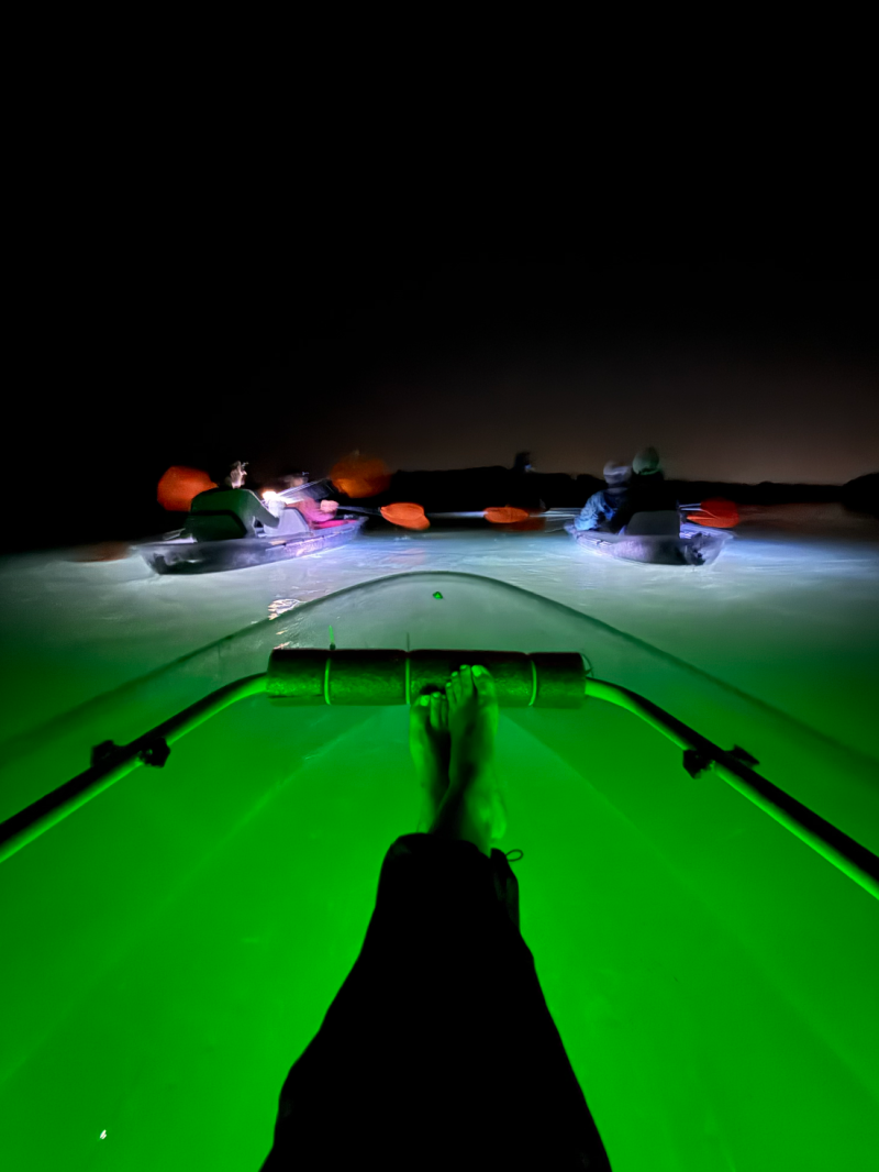 Person relaxes on a boat at night with green glow and others in distance.