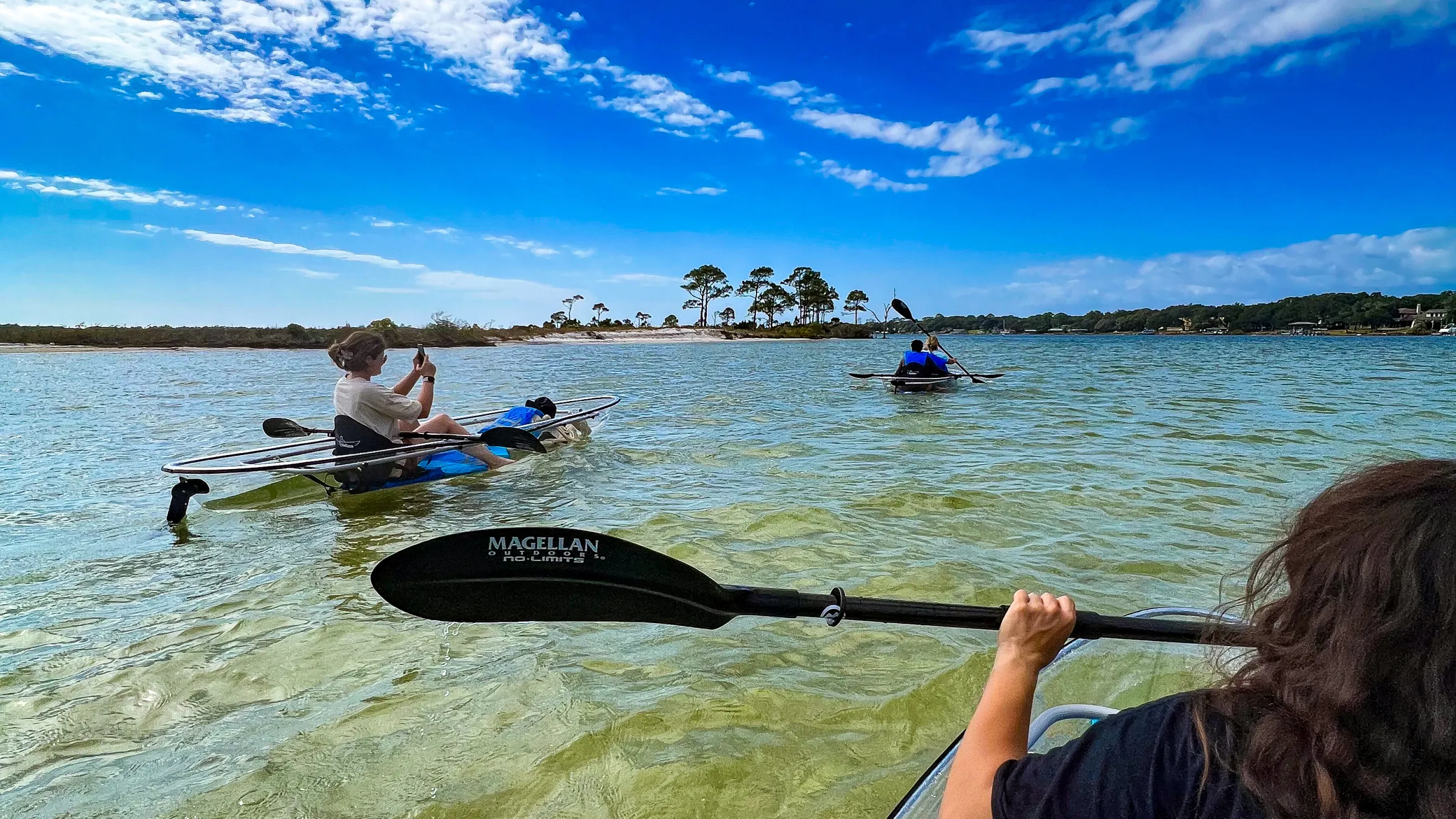 Kayakers paddling in clear water under a blue sky with clouds.