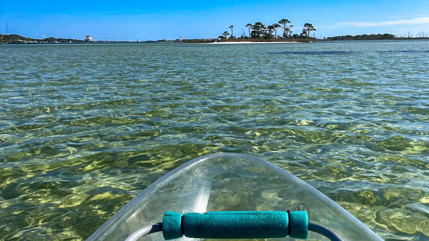 Clear kayak on shallow, transparent water with an island in the distance under a clear blue sky.