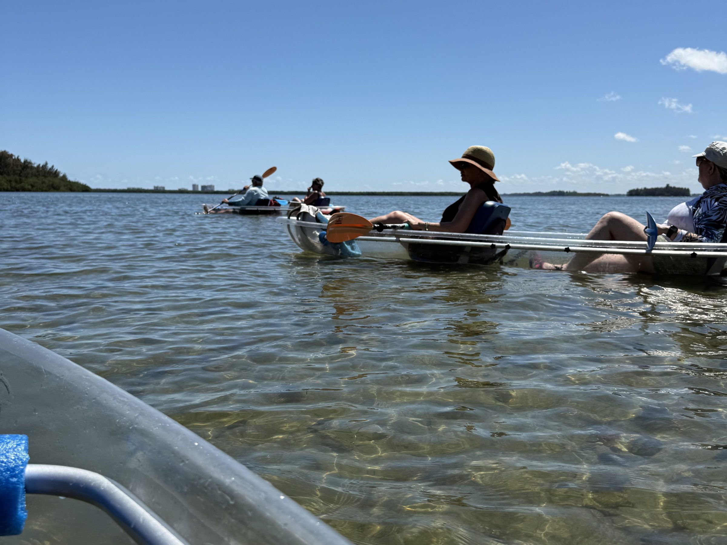 People kayaking on shallow, clear water under a sunny sky.
