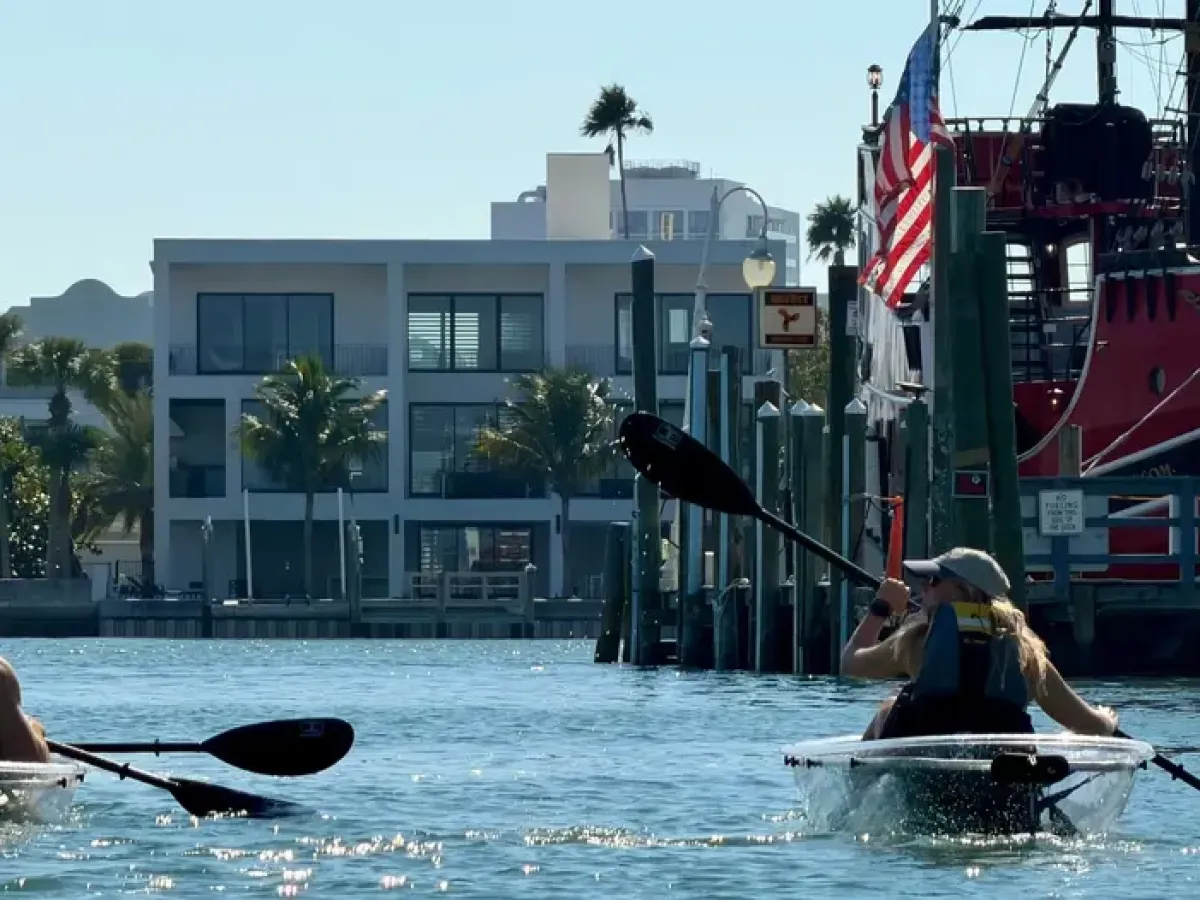 Two people kayaking near a docked red ship on a sunny day.