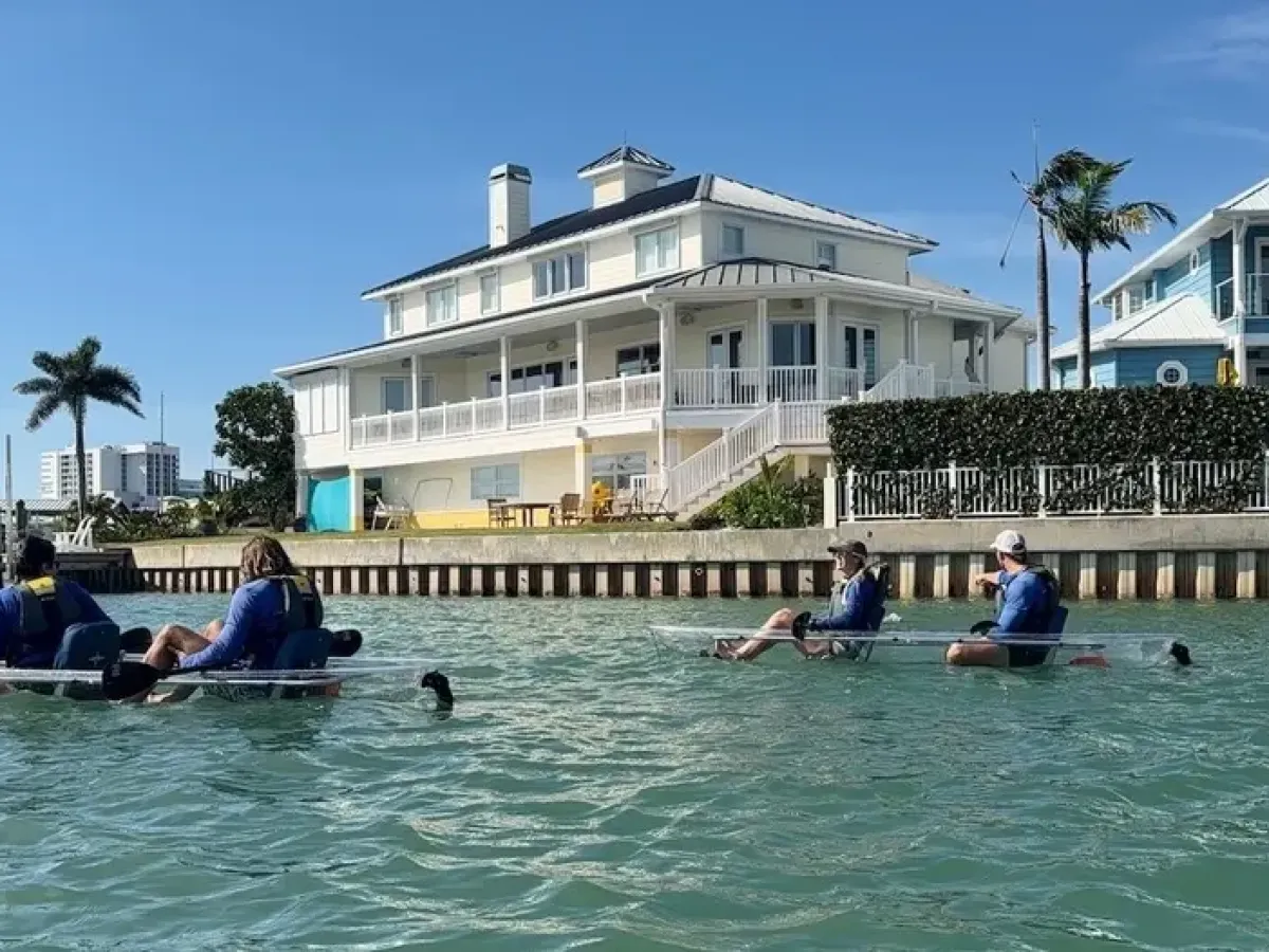 People kayaking on water with houses and palm trees in the background.