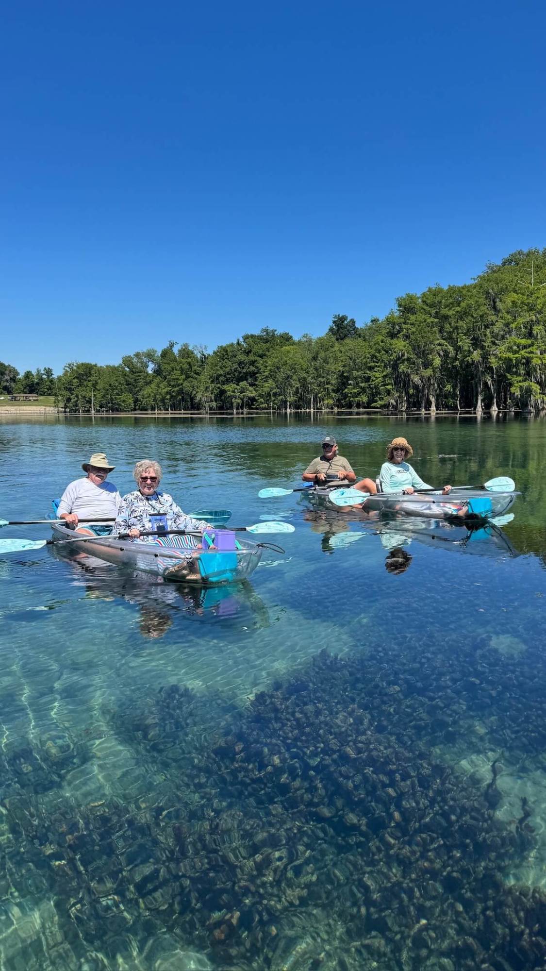 Four people kayaking on clear water under a blue sky.