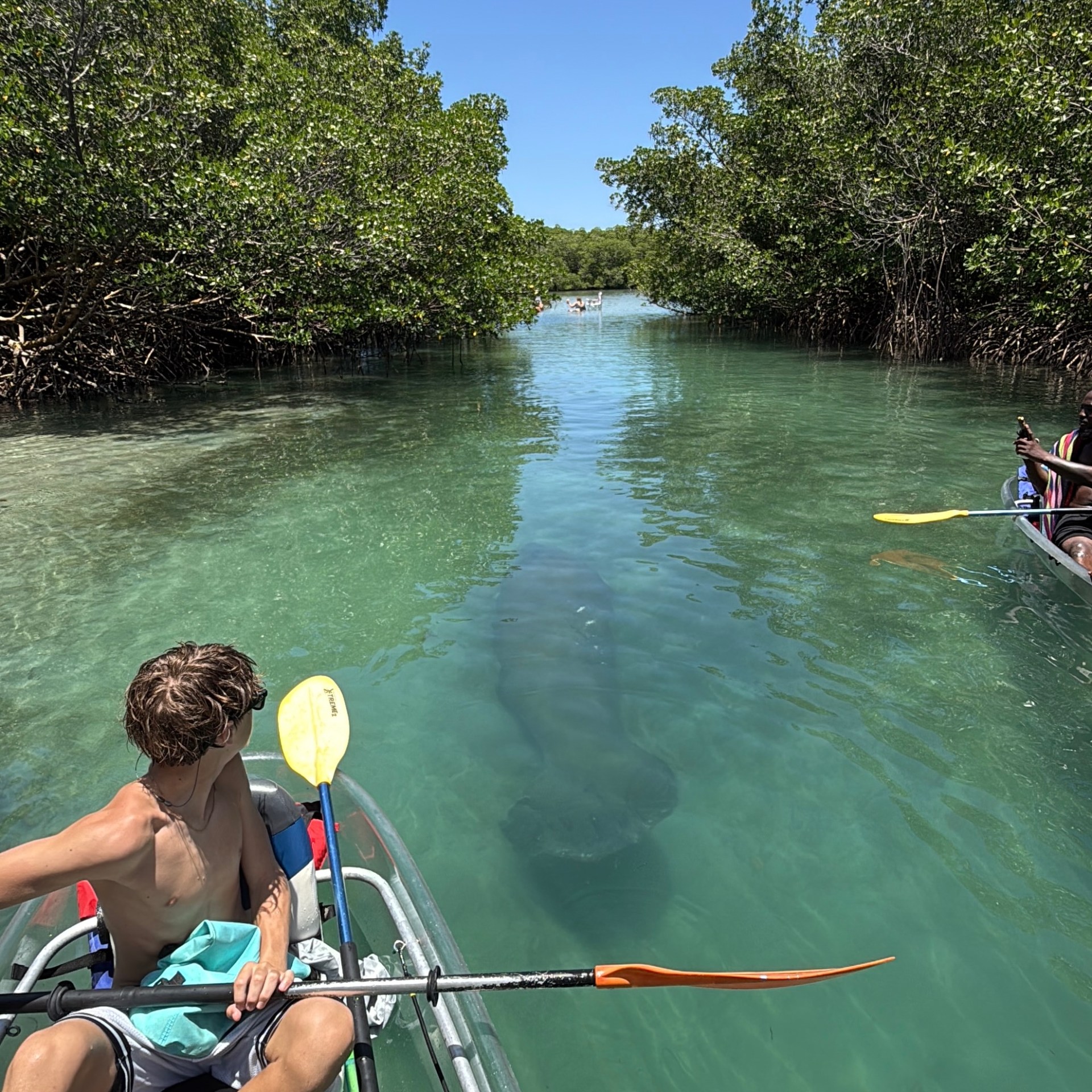 Boy in kayak on clear water with a shadowy figure beneath.