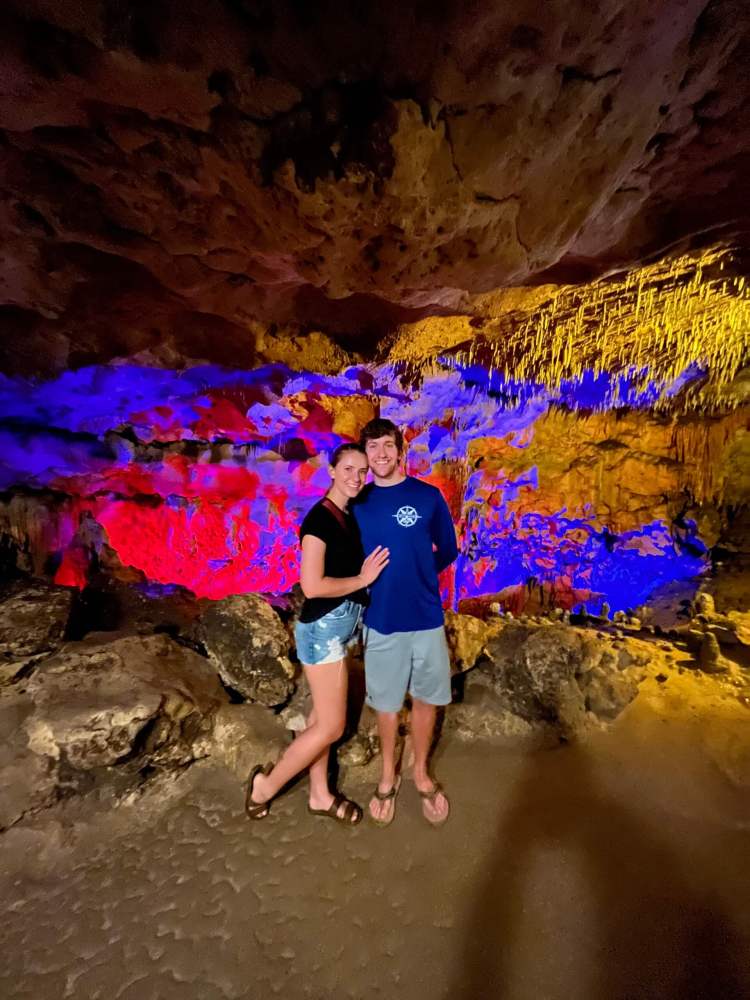 Couple posing in a colorful, illuminated cave with stalactites.