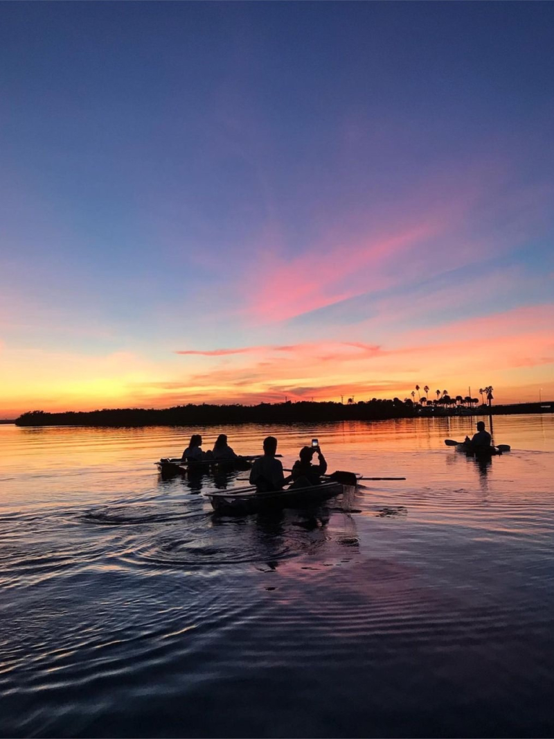 Silhouetted kayakers on a lake at sunset with colorful sky.