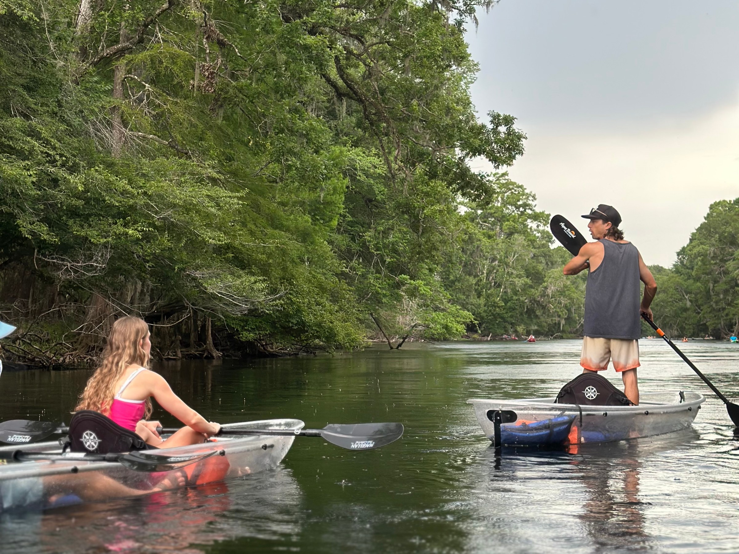 People kayaking on a calm river surrounded by lush trees.