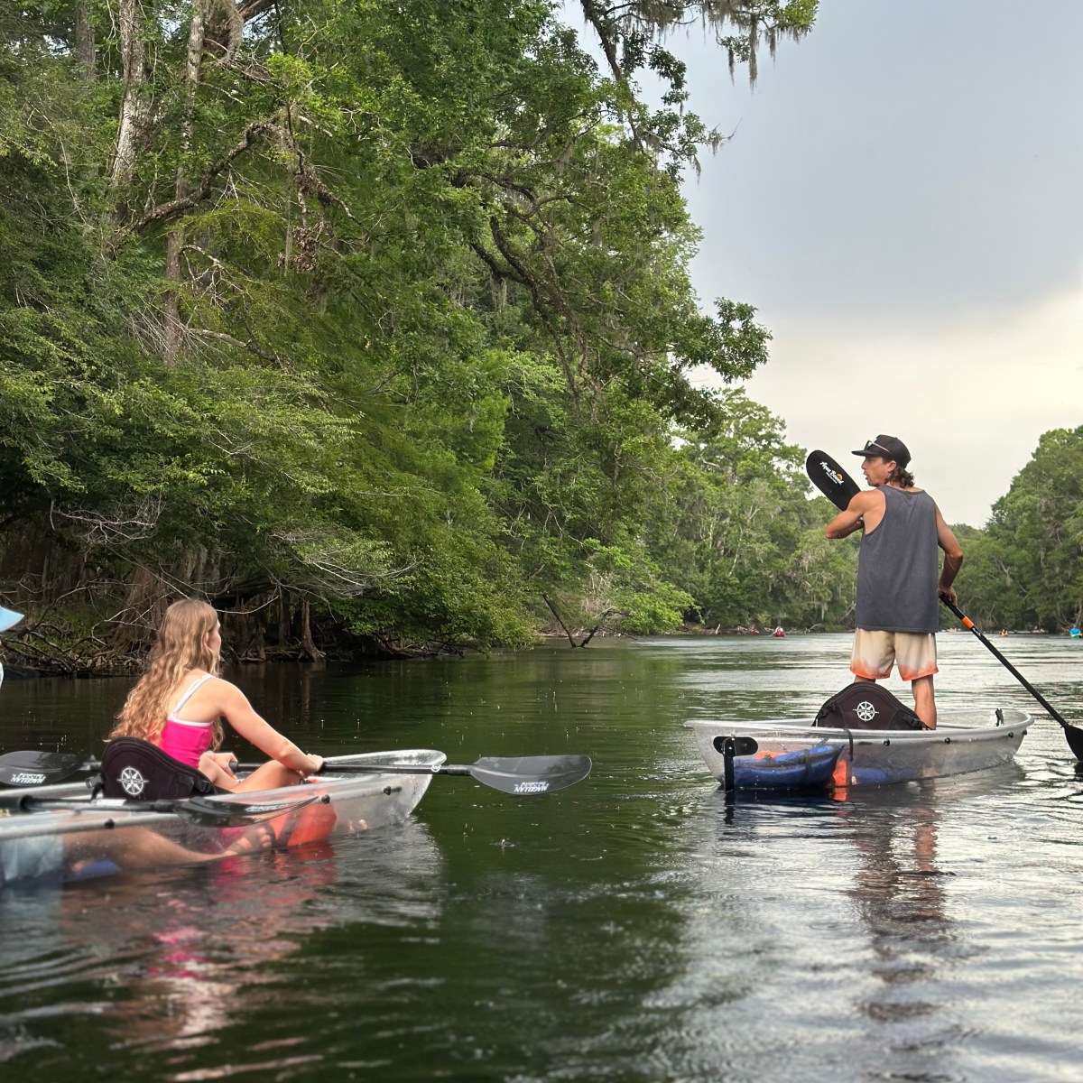 People kayaking on a calm river surrounded by lush trees.