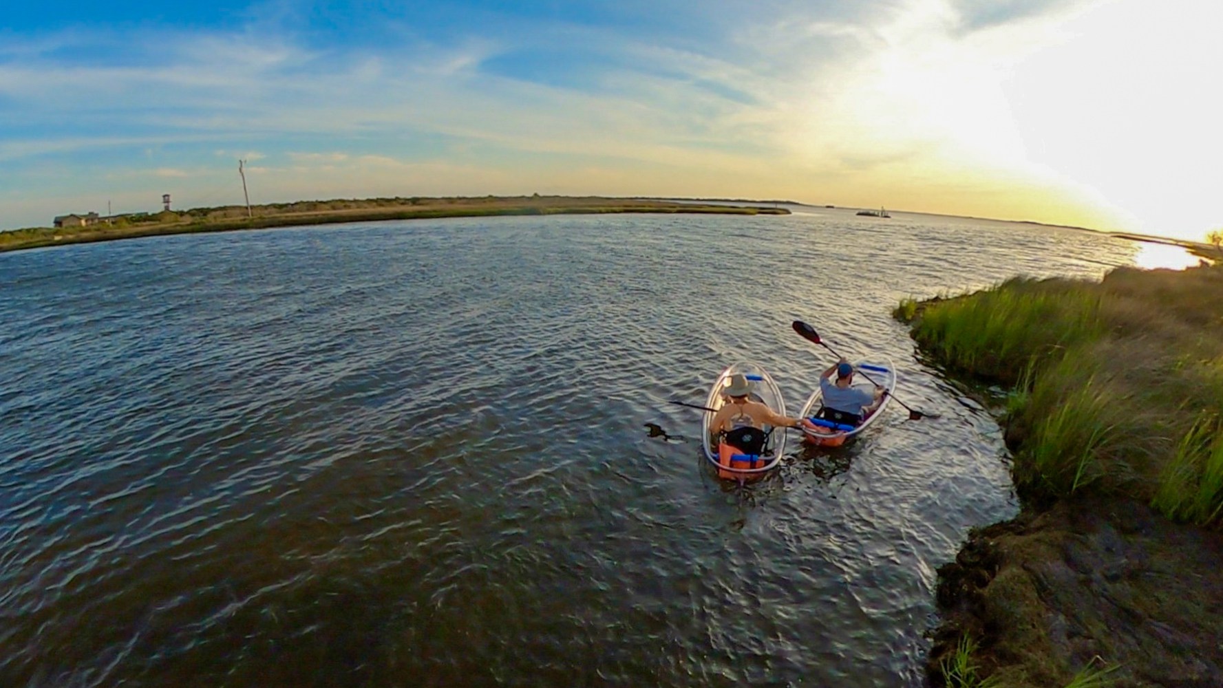 Two kayaks on a calm river near grassy shore at sunset.