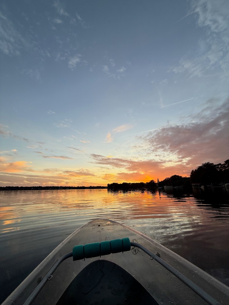 Kayak on a calm lake at sunset with colorful sky and reflections.