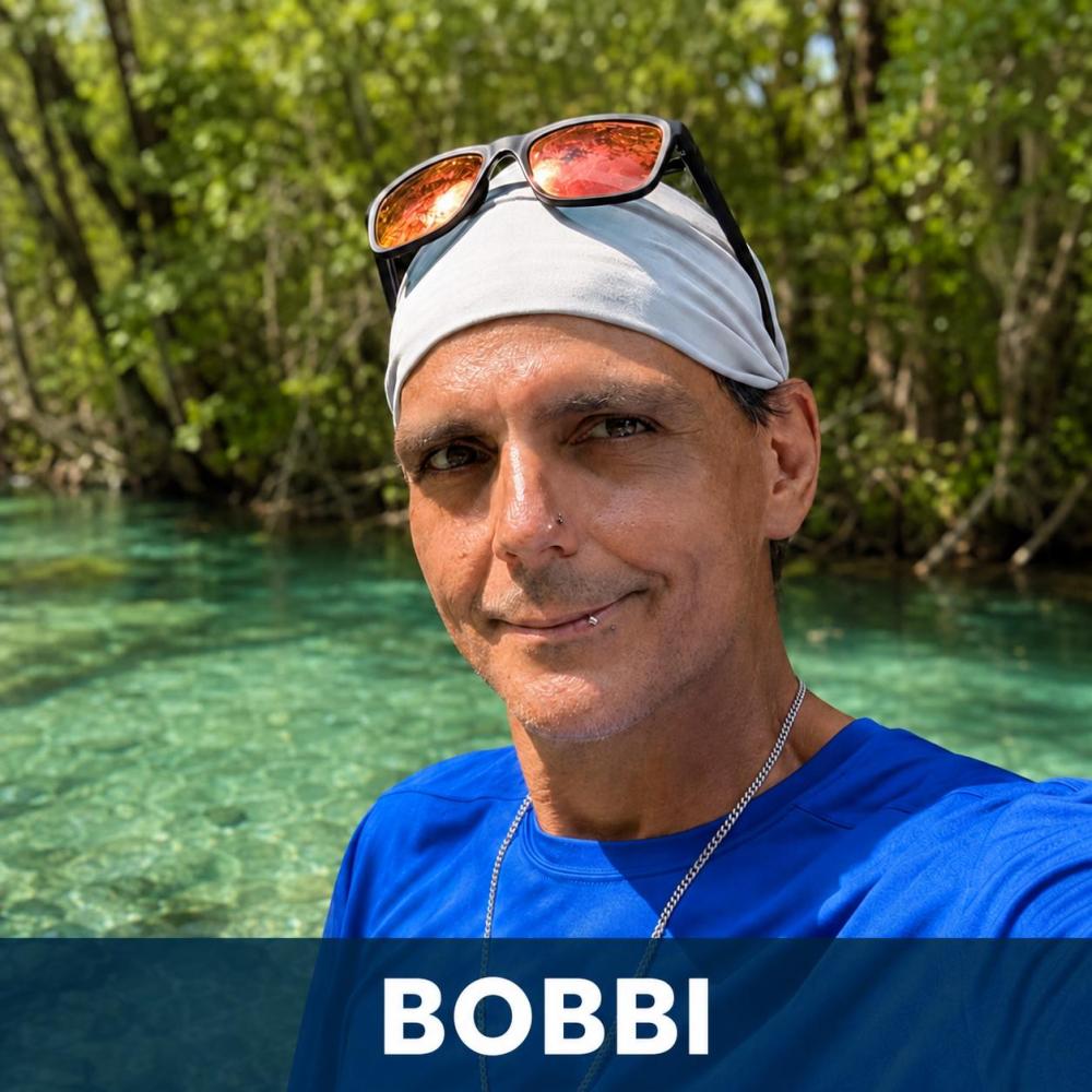 Man in blue shirt with kayaks and trees in the background.