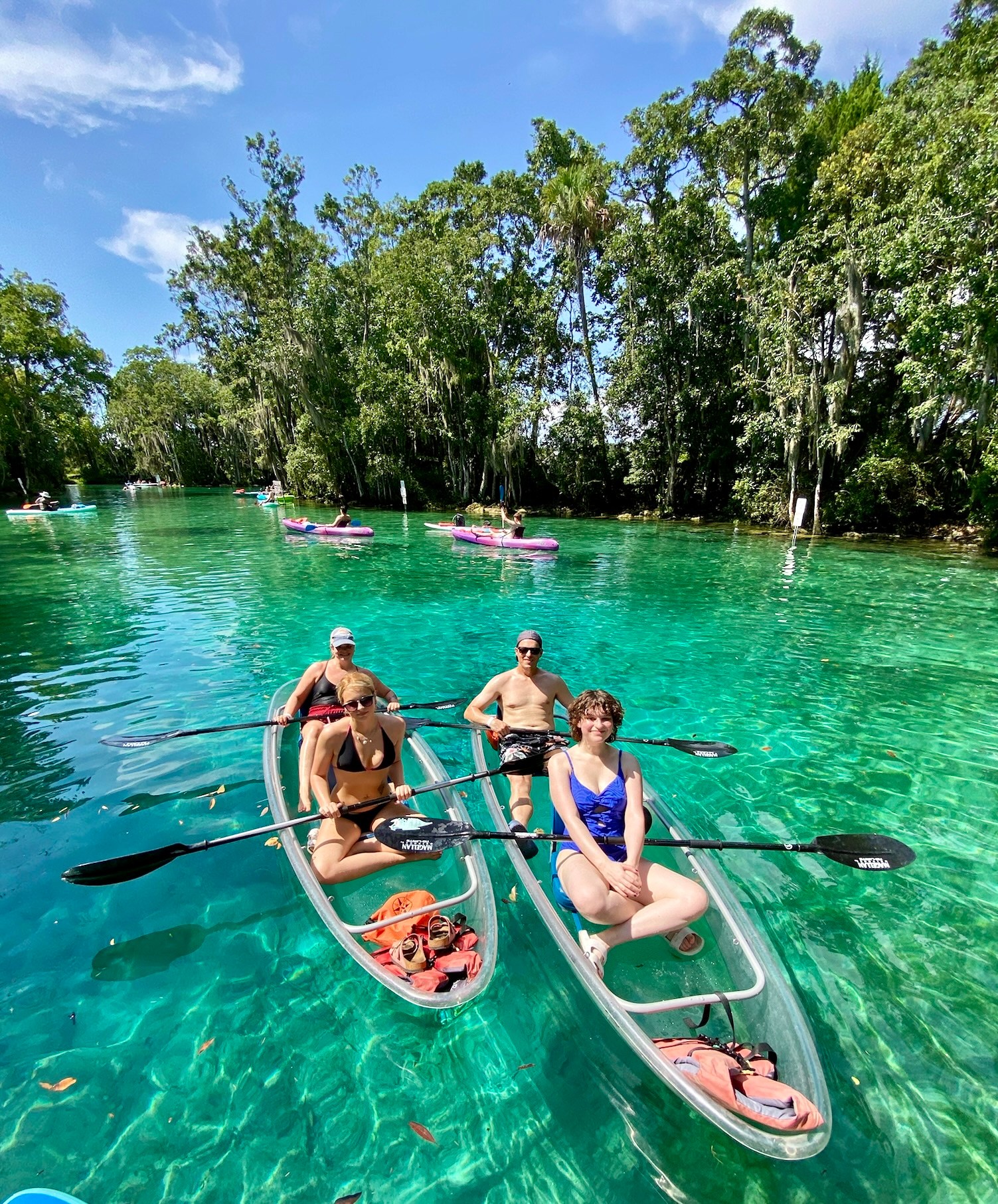 Four people kayaking on a clear blue river with surrounding trees.