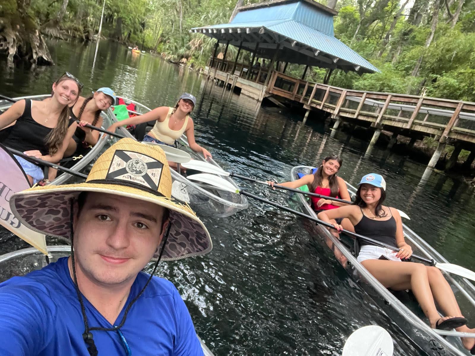 Group kayaking on a river near a wooden dock and pavilion.