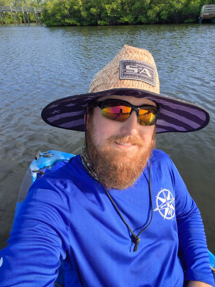 Person wearing a large straw hat and sunglasses on a boat, smiling at the camera.