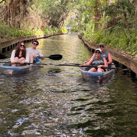 Four people canoeing on a lush, tree-lined canal.