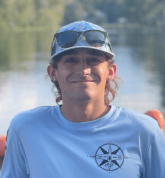 Person in blue shirt and cap smiling, standing near water.