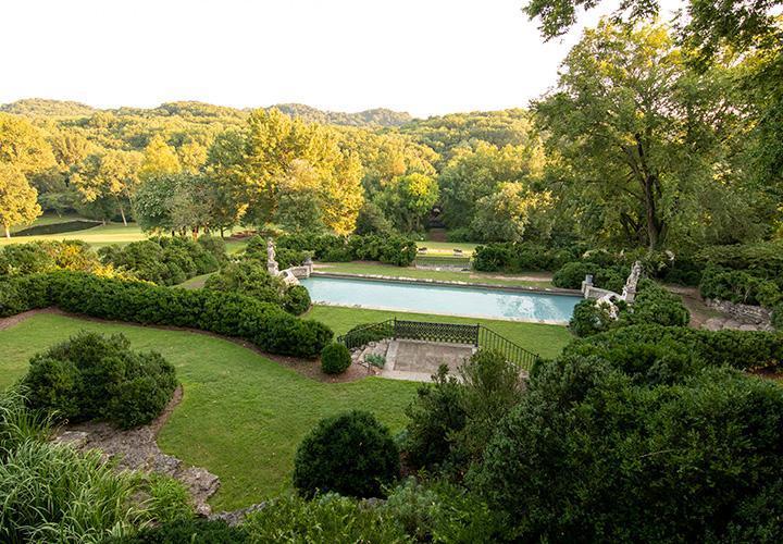 Lush garden with pathway, rectangular pool, surrounded by trees and bushes.