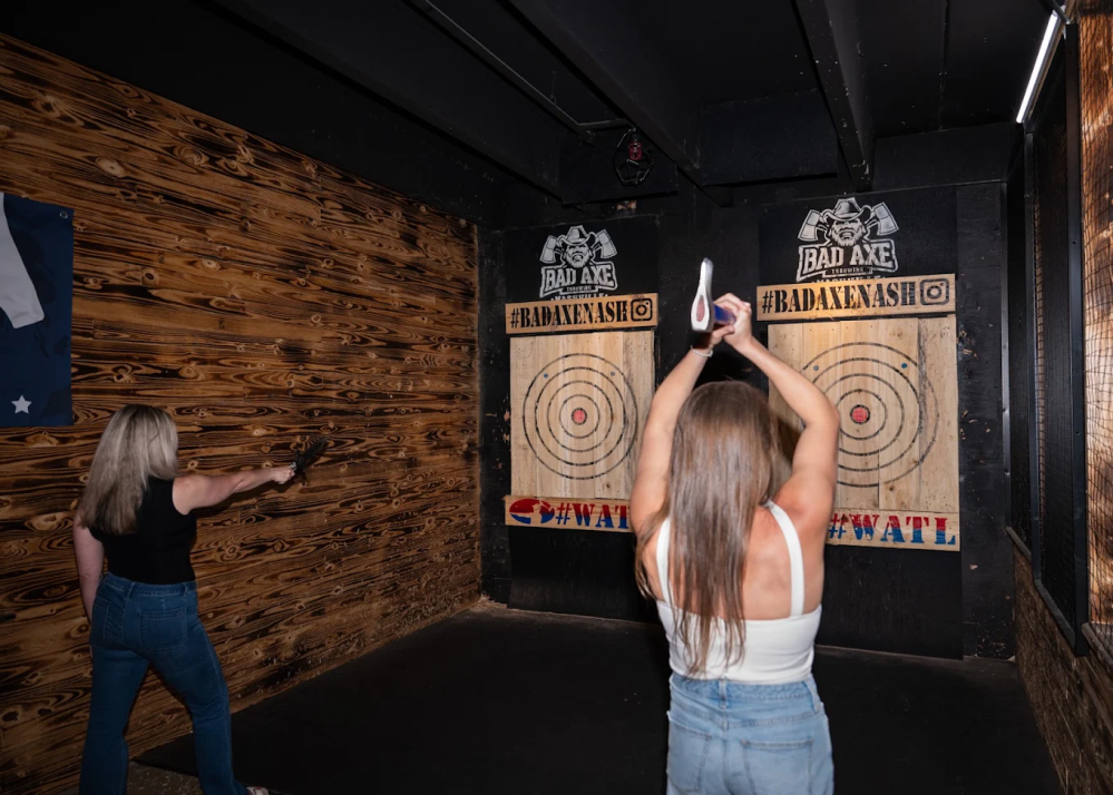 Two people throwing axes at targets in an indoor range.