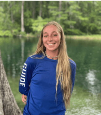 Smiling person in a blue shirt stands by a pond.