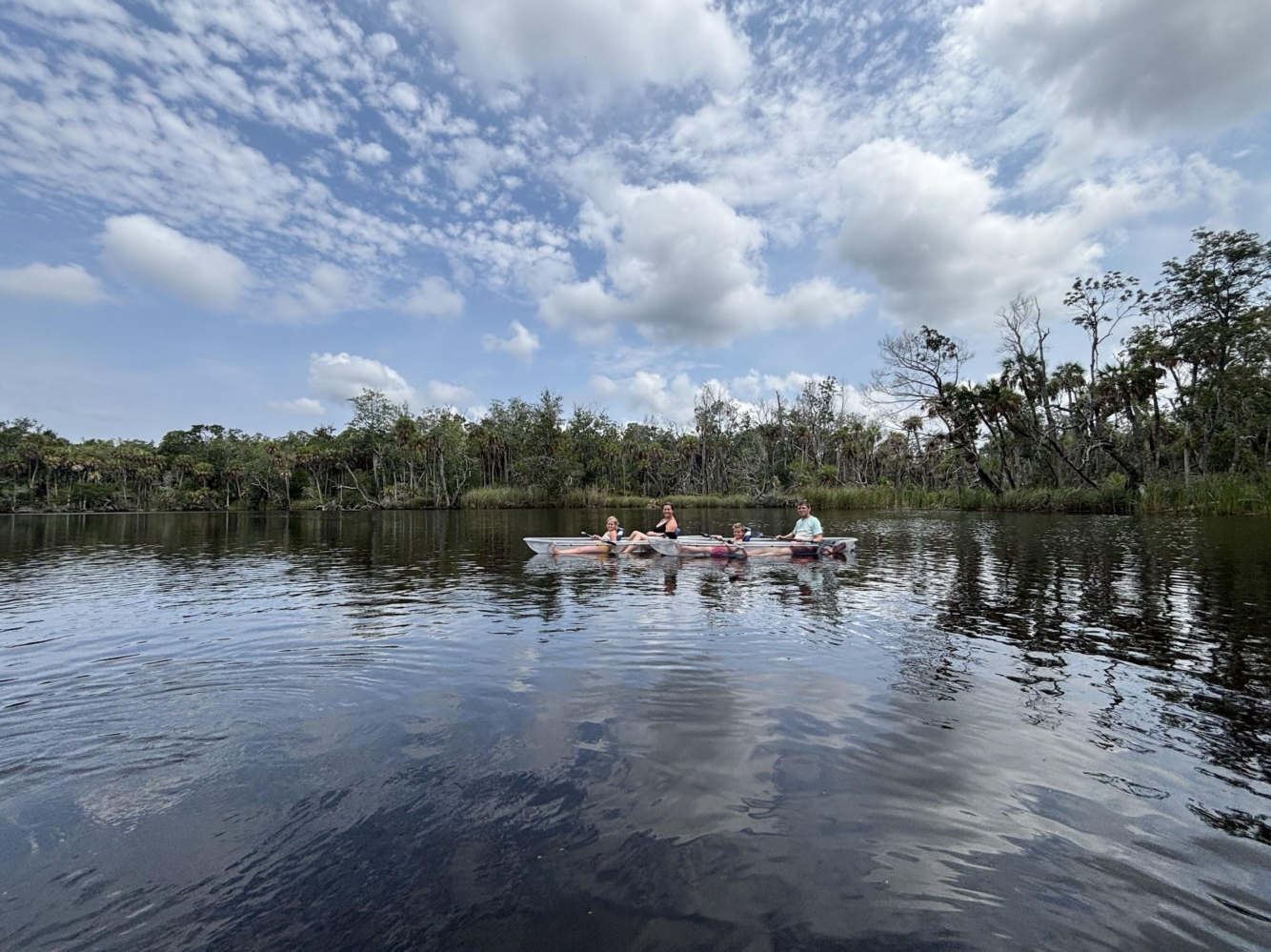 People kayaking on a calm lake under a cloudy sky with trees in the background.