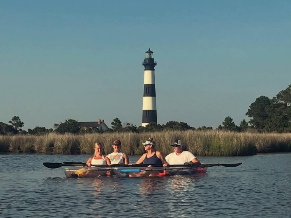 Four people kayaking on water with a striped lighthouse in the background.