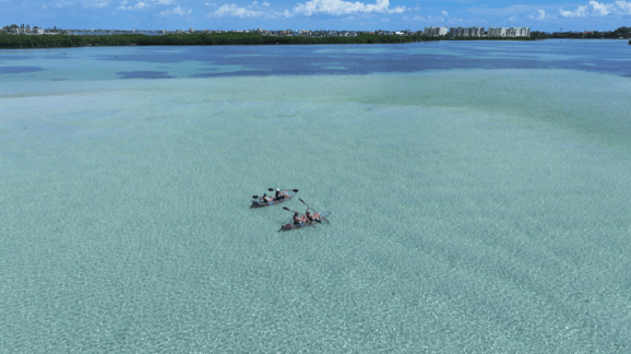 Group of people lounging on a sandbar in clear blue water.