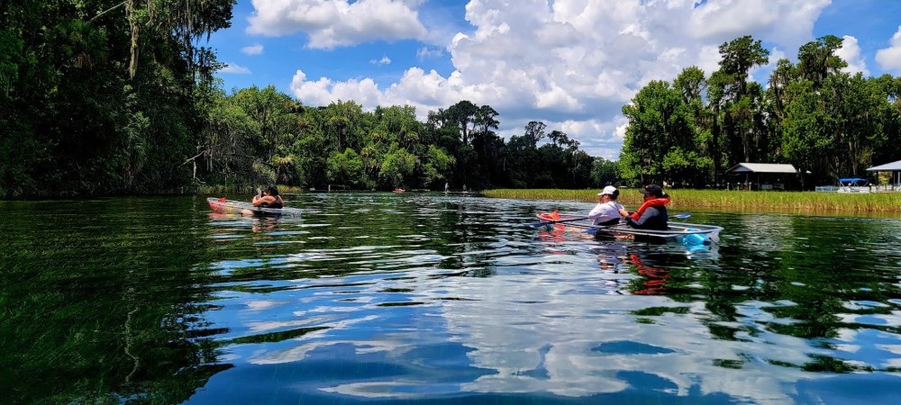 People kayaking on a calm river under a partly cloudy sky.