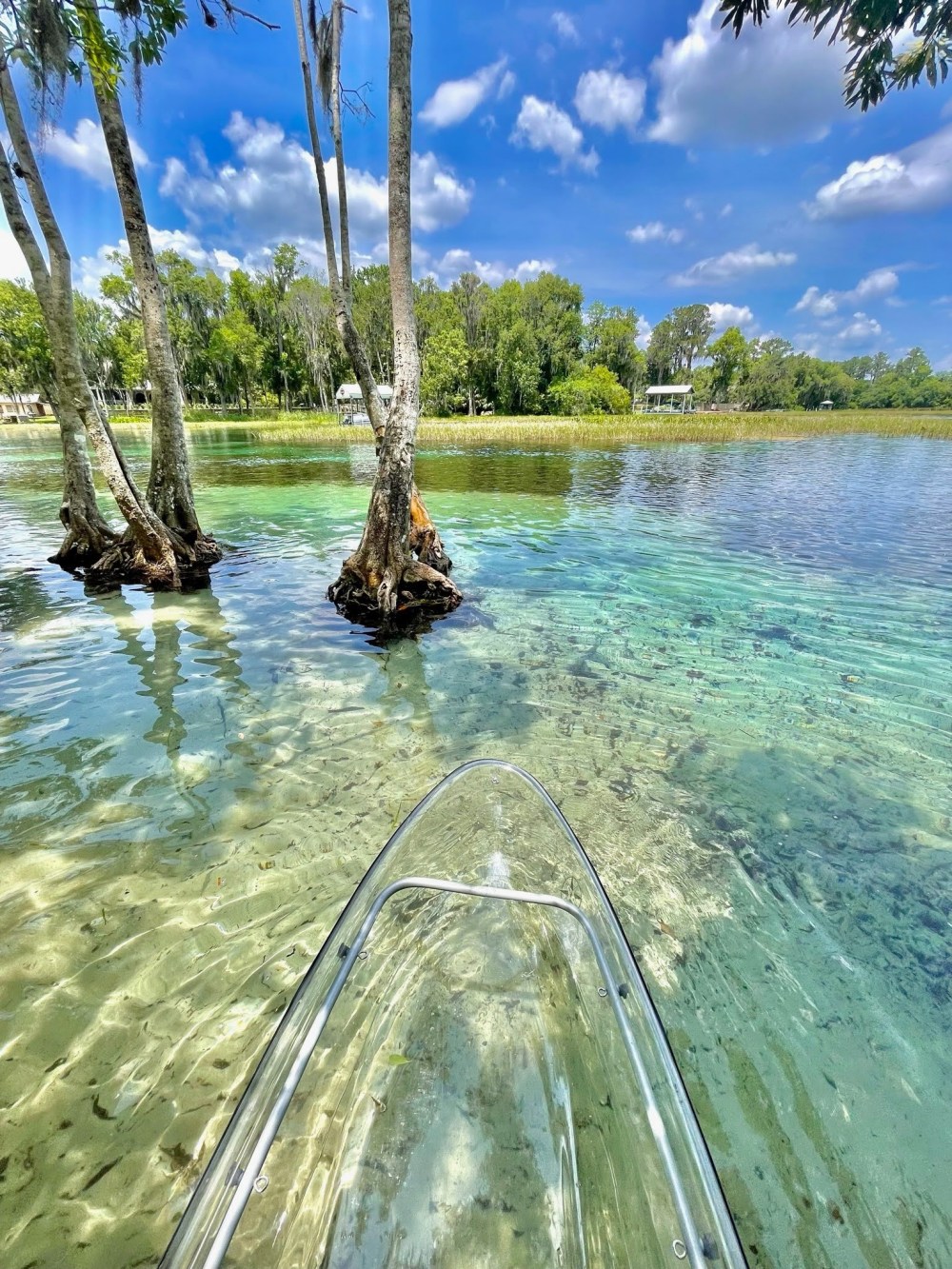 Clear kayak on crystal-clear water near trees with a blue sky and clouds.