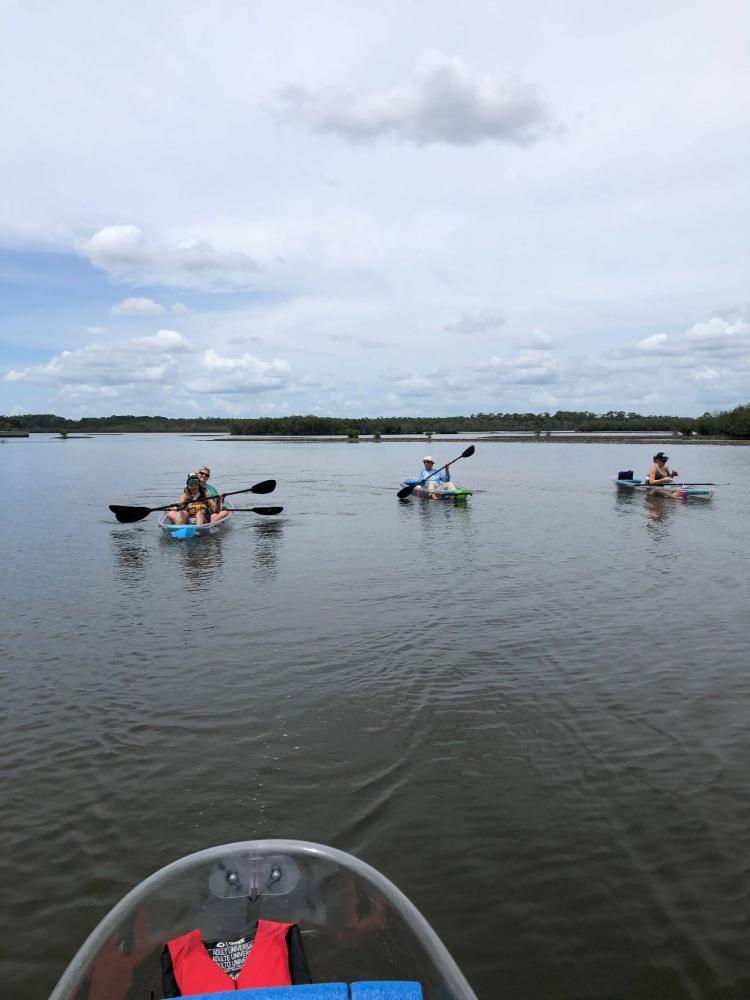 Three people kayaking on a calm lake under a cloudy sky.