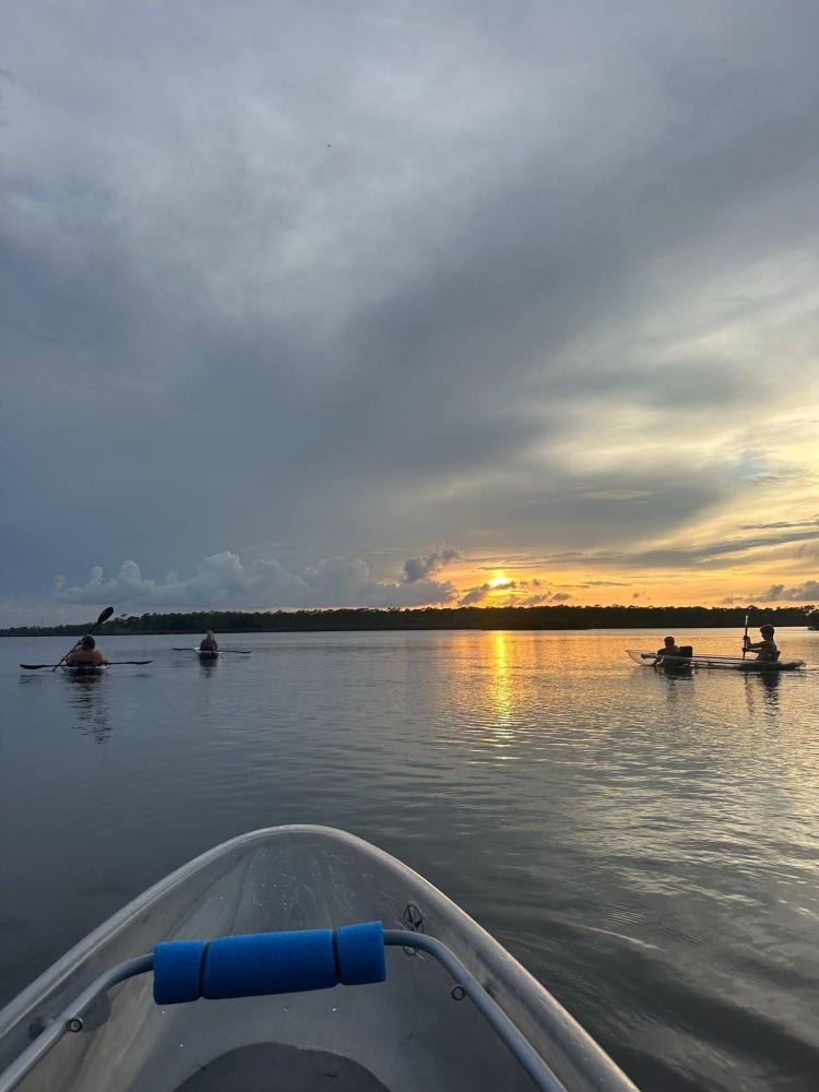 Kayaks on a calm lake at sunset with cloudy sky.
