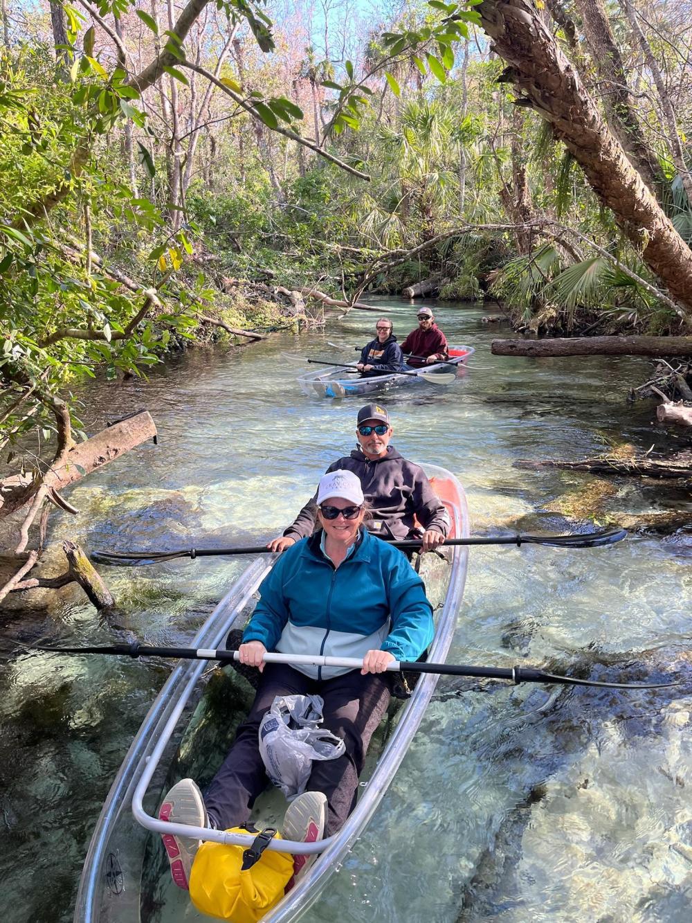 Guests paddling clear kayaks along a tree-lined creek at Rainbow Springs